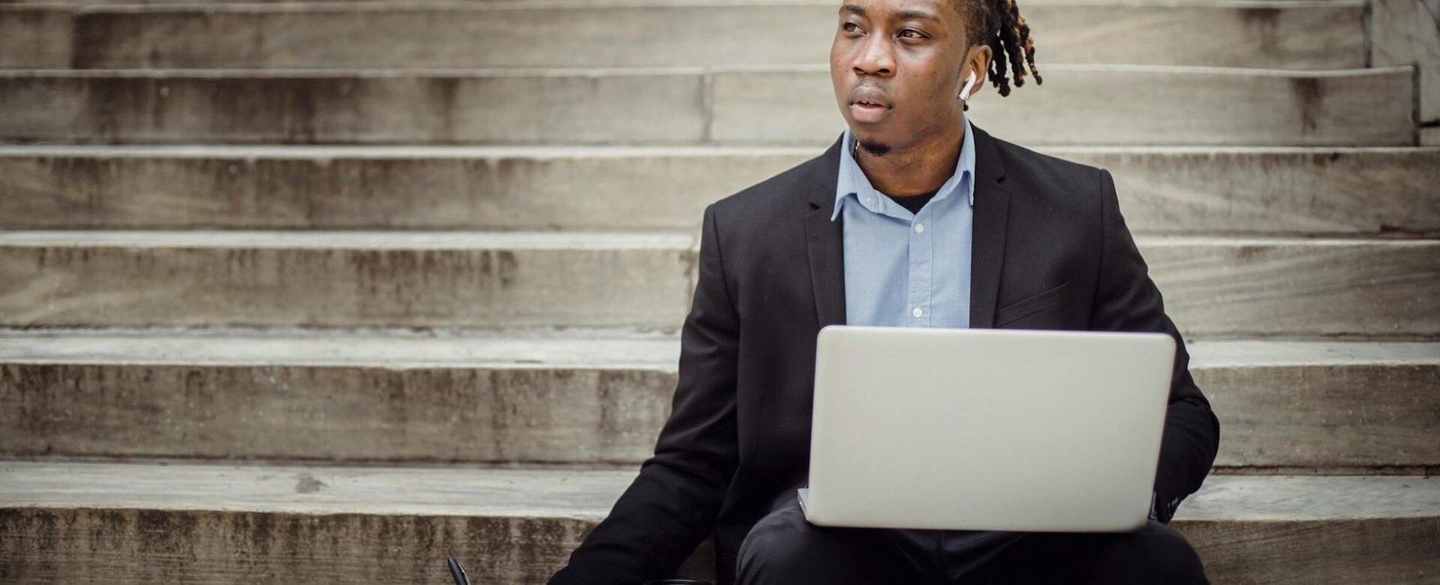 thoughtful black worker using netbook and taking notes sitting on steps